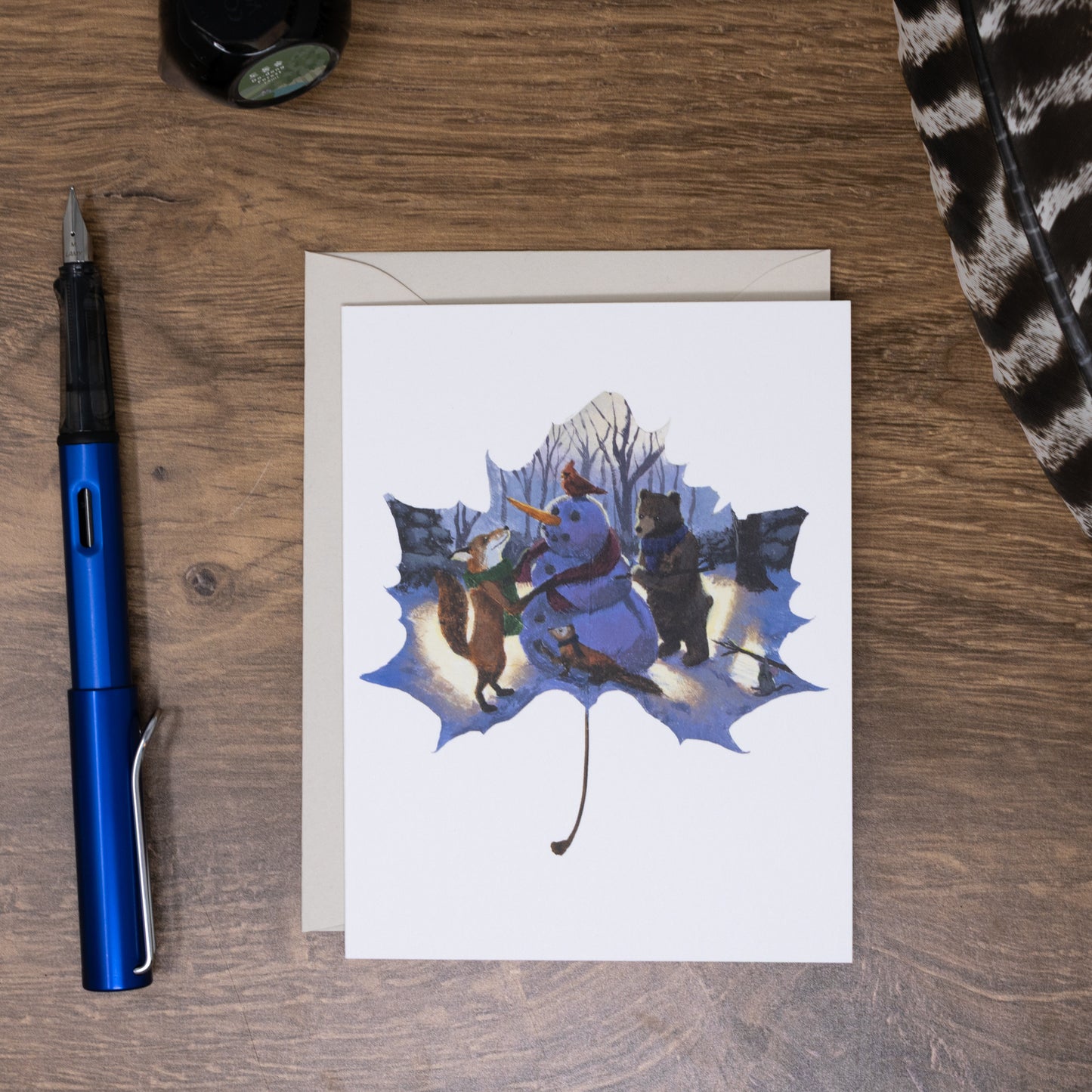 Greeting card with winter scene illustration on a wooden surface with a pen.