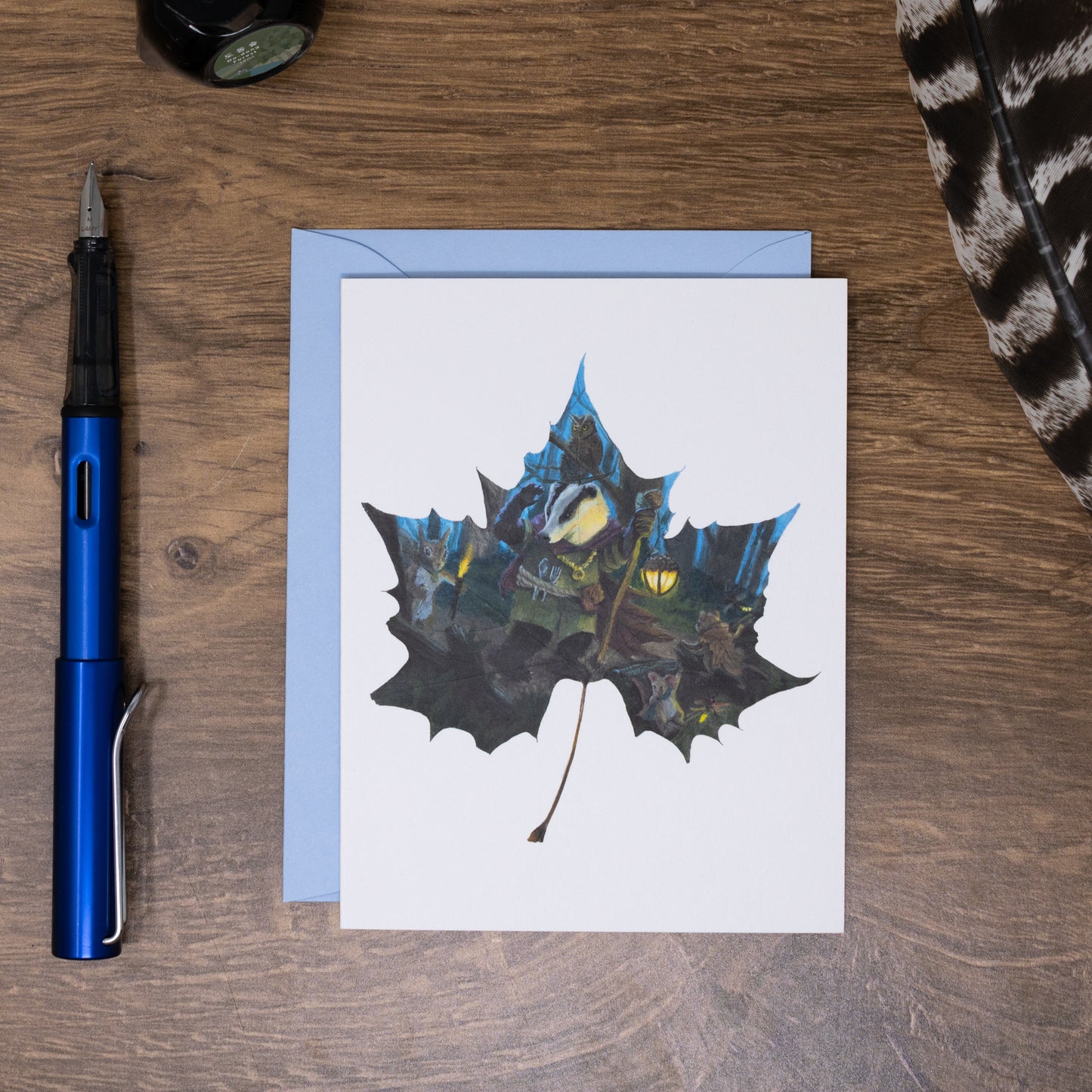Greeting card with leaf design on a wooden surface with a pen and feather.