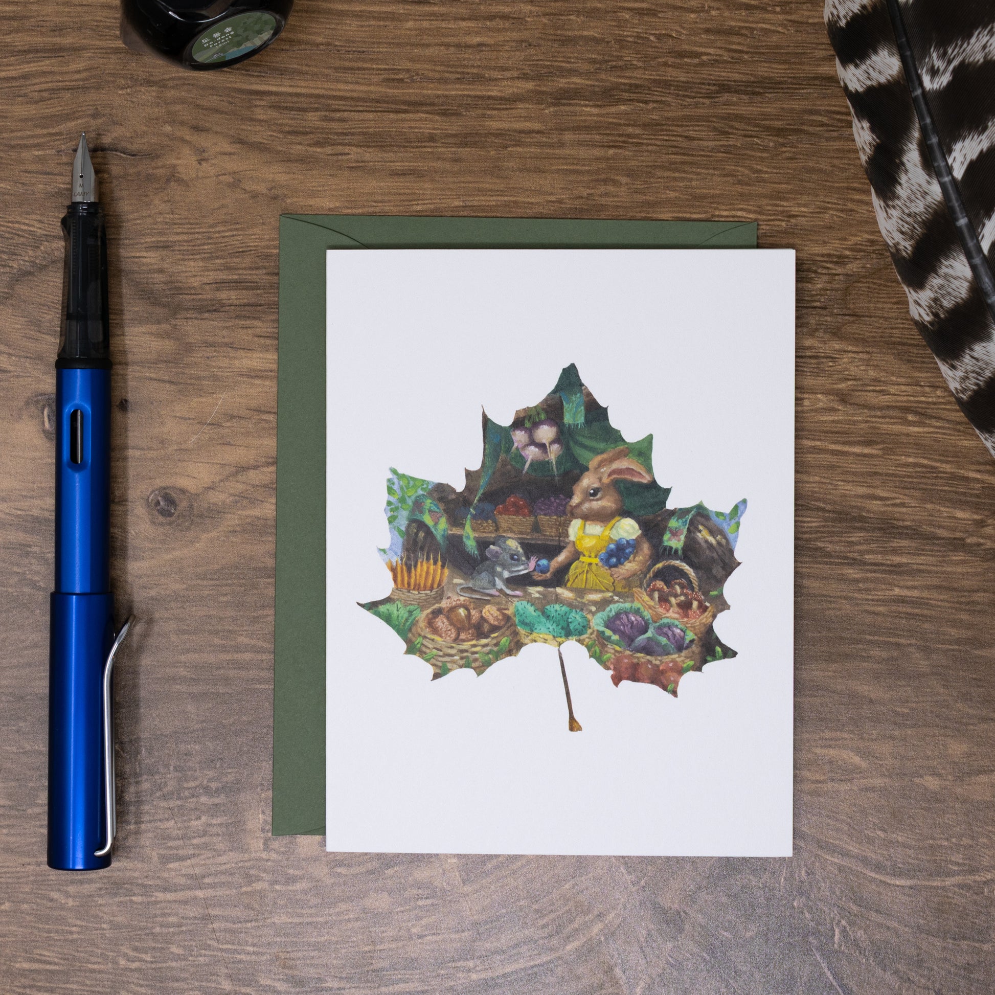 Greeting card with leaf design on a wooden surface with a pen and other items.